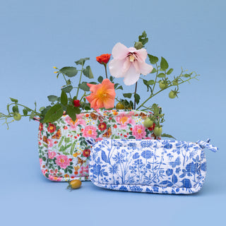Two fabric zip pouches displayed on a light blue background, styled with flowers. The pouch in the back features a multicolor floral print, and the pouch in the front features a blue botanical pattern on a white background.