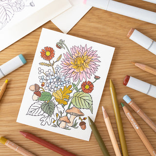 Coloring book page (greeting card) with floral design on a wooden table with coloring supplies.