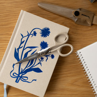 Notebook with blue floral design and scissors on a wooden surface