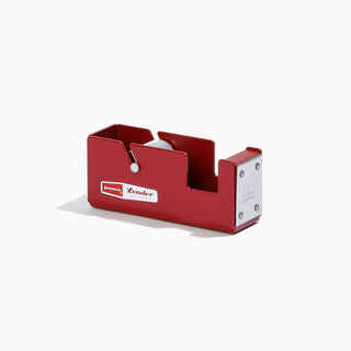 A red metal tape dispenser with a white roll of tape inside, featuring a white 'TapeLeader' logo on the front and a silver metal mounting bracket on the side, set against a plain white background.