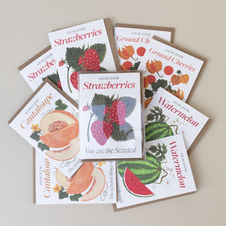A fan arrangement of illustrated fruit-themed greeting cards on a light beige background. Visible designs include strawberries, cantaloupe, ground cherries, watermelon, and a central strawberry card reading 'You are the Sweetest.