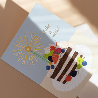 Macro detail of Make A Wish Birthday Cake greeting card highlighting the delicate watercolor textures and luxurious gold foil accents that enhance the magical birthday wish theme on premium matte cardstock