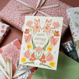 Detail of Birthday greeting card by Oana Befort for Botanica Paper Co. featuring spring florals with gold foil accents and gift wrap in the background