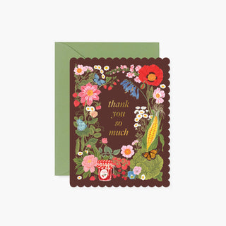A floral thank-you card with a scalloped dark brown border, featuring colorful flowers, a corn cob, butterflies, and the words 'thank you so much' in gold. The card is shown with a sage green envelope behind it on a light gray background.
