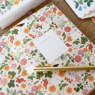 Reverie planner opened to reveal beautifully illustrated interior covers featuring lush florals in soft pinks, greenery, and pastels by Oana Befort for Botanica Paper Co., showcasing the lay-flat binding design