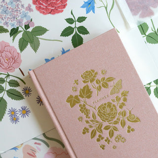 Reverie planner artfully styled with original painted botanical artwork in the background by Oana Befort for Botanica Paper Co., showcasing the inspiration behind the lush floral designs and soft pastel color palette