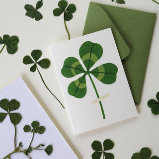 Four leaf clover card and pressed clovers on a light cream background and green envelope.