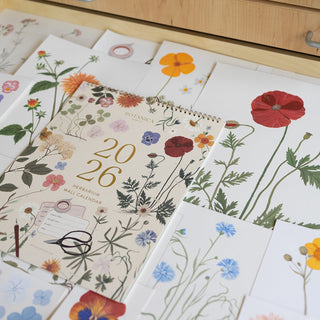 2026 Herbarium calendar styled with original botanical watercolor paintings by artist Oana Befort shown in the background.