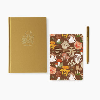 Linen-bound journal, a notebook, and a pen on a white background, one with a gold cover and the other with a mushroom pattern.
