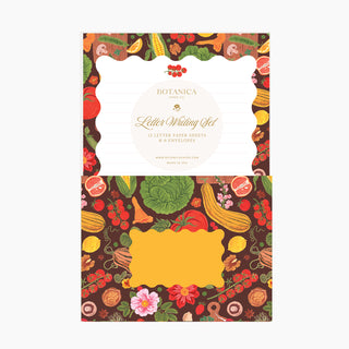A letter writing set card set by Botanica Paper, featuring a dark brown background decorated with colorful illustrations of fruits, vegetables, and flowers. The set includes a white card with lined writing space and a yellow card template, all framed by the patterned border.
