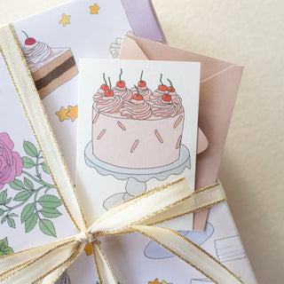 Mini greeting card with a cake illustration tied with a ribbon, surrounded by other cards.