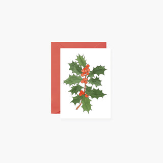 A white greeting card featuring an illustration of green holly leaves with red berries, shown with a coral-red envelope behind it on a light gray background.