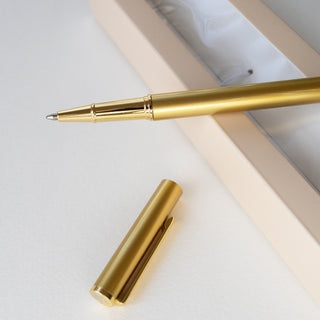 Gold pen and cap on a light gray surface