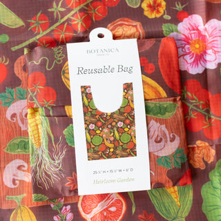 A reusable tote bag by Botanica Paper Co. in a vibrant botanical print, shown with its white hang tag on top of another matching bag.