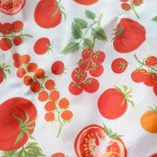 A close-up of a white ripstop shopping bag with a repeating print of red tomatoes and green leaves, including whole tomatoes, clusters on the vine, and a tomato slice.