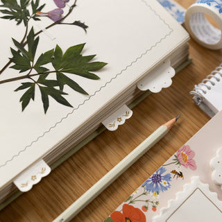 Notebook with floral and leaf designs and sticky note tabs on a wooden surface with a pencil.
