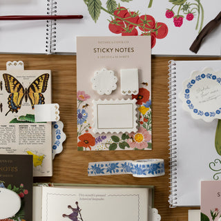 Collection of stationery items including sticky notes, notebooks, and decorative elements on a wooden surface.