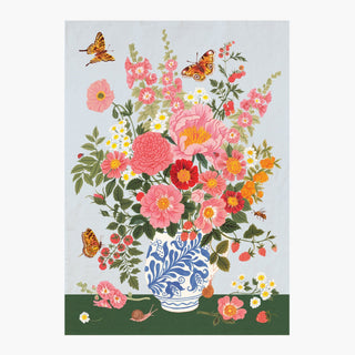 A botanical tea towel featuring a vibrant Romanian folk ceramic vase of pink, red, and orange flowers in a blue and white patterned vase, with butterflies and small white daisies on a pale blue background and dark green base.