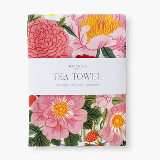 A Botanica Paper Co linen Tea Towel with a vibrant floral print featuring pink flowers, yellow centers, and green leaves, wrapped in a white paper band with the brand name and product type printed on it.