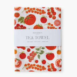 A Botanica Paper Co tea towel with a white linen background and a vibrant red tomato and cherry tomato pattern, wrapped in a white paper band.