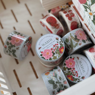 Several rolls of washi tape with floral and botanical illustrations are arranged in a white slatted tray. The labels read 'BOTANICA PAPER CO.