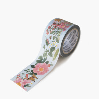 A roll of washi tape with a botanical pattern featuring pink flowers, green leaves, and small bees on a pale blue background, shown on a clean white studio background.