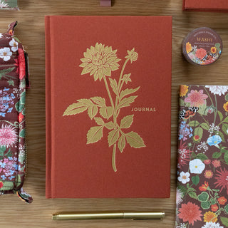 Red journal with floral design and 'Journal' text on a wooden surface with floral items.