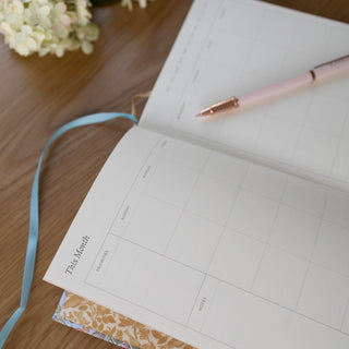 Top-Side view of Songbirds Linen Bound Planner illustrated by Oana Befort for Botanica Paper Co. showing the This Month page.