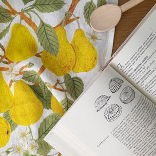 Botanica Paper Co.'s Pear Orchard linen tea towel hanging gracefully in a bright kitchen, showcasing the charming fruit tree artwork that brings orchard beauty to everyday culinary moments