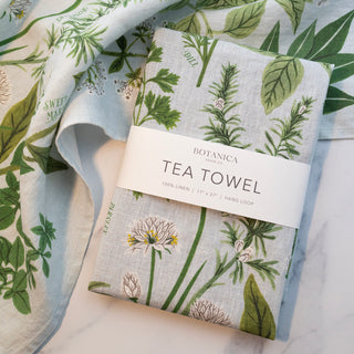 Botanica Paper Co.'s Herb Garden linen tea towel displayed on a kitchen counter, showcasing the elegant herb botanicals that bring garden-fresh charm to culinary spaces and cooking rituals